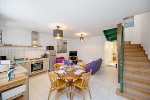 A modern kitchen with a dining area, a staircase, and a living room with a sofa. - L’Escapade Lanvollonnaise - Plage à 15 min (Lanvollon)