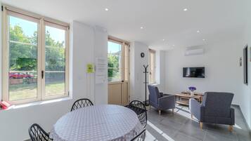 A modern living room with a dining area, large windows, a flat-screen TV, and a coat rack.