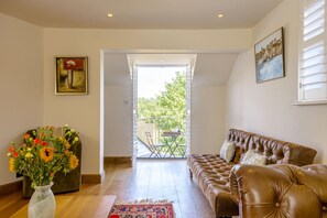 A living room with a brown leather sofa, a vase of flowers, and a painting on the wall.