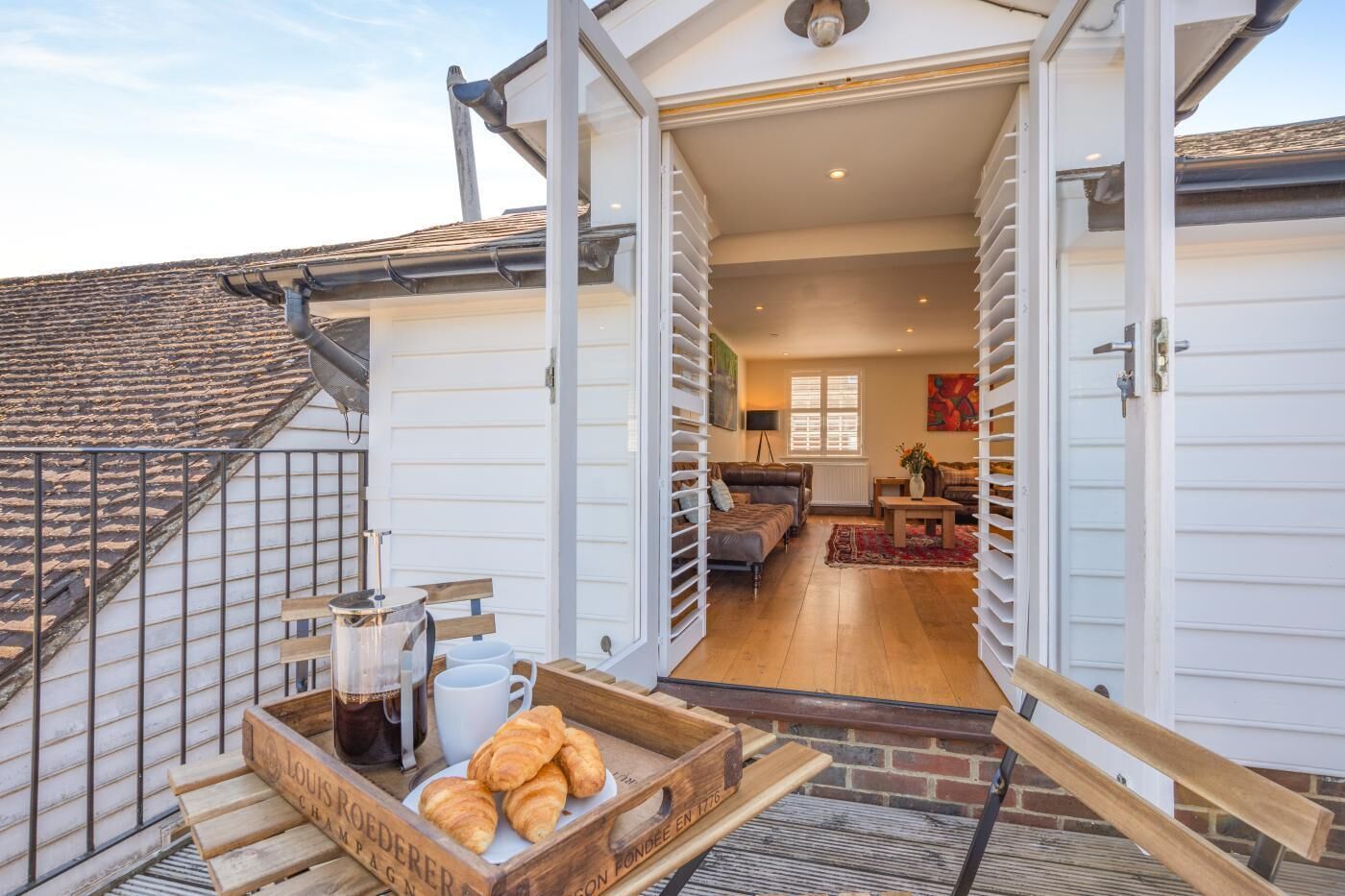Un appartement de style « loft » avec un escalier menant à un balcon, un coin repas avec un plateau de croissants et du café, et un salon avec un canapé et une table.
