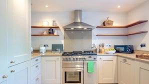 A modern kitchen with a gas stove, oven, and microwave. There are wooden shelves with kitchen items and a basket.