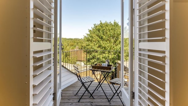 A balcony with a table and chairs, overlooking a garden and trees.