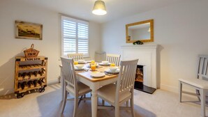 A dining room with a wooden table set for four, white chairs, a basket labeled 'P&M INDUSTRY', and a fireplace with a mirror above it.