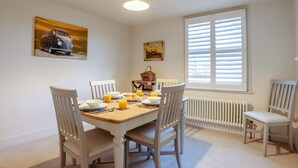 Een eetruimte met een tafel voor vier personen, stoelen, een radiator en een raam met zonwering.