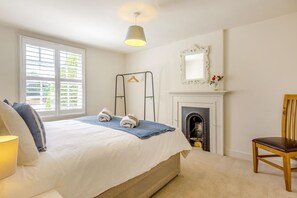 A bedroom with a bed, a chair, a hanging light fixture, a fireplace, and a window with blinds.