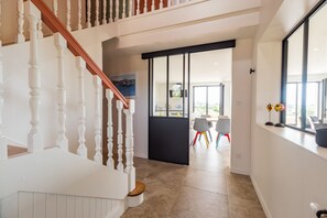 Ein modernes Interieur mit einer Treppe, einer Essecke mit Stühlen und einem großen Fenster.