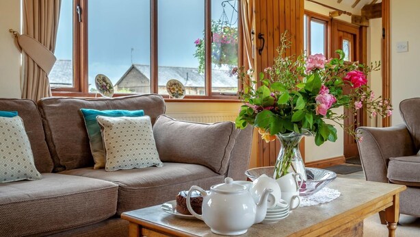 A cozy living room with a sofa, a coffee table with a teapot and cups, and a vase with flowers. - 2 Bed in Stratford -upon- Avon (oc-cc009) (Welford-on-Avon)