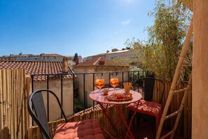 Ein Balkon mit Tisch für zwei Personen, gedeckt mit Getränk, Speisen und einer kleinen Oliven-Schale.