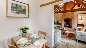 Un comedor con una mesa dispuesta para cuatro personas, un cuadro en la pared y vista a una sala de estar con chimenea.