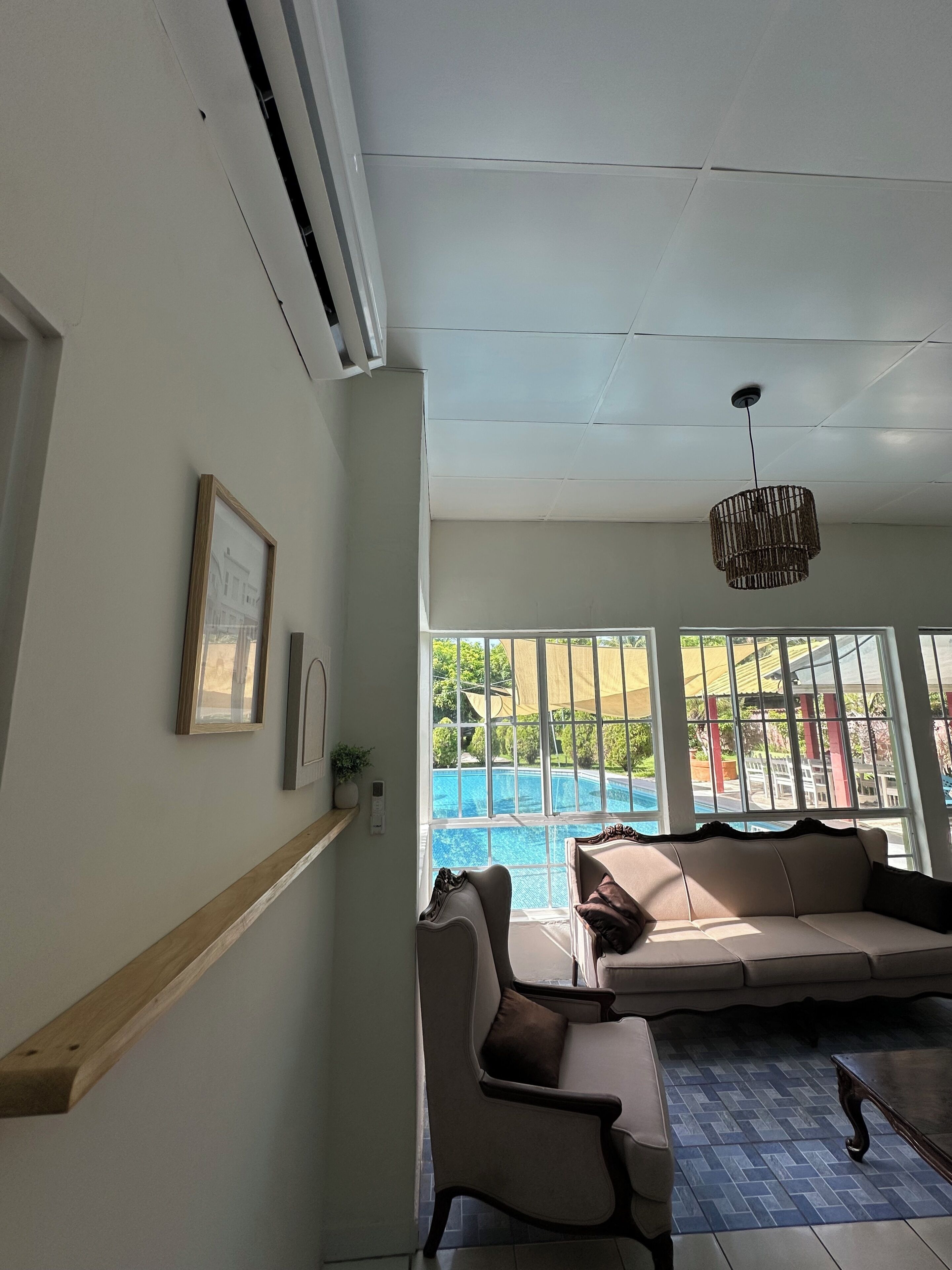 A room with a sofa, a chair, a hanging light fixture, and a window with a view of a swimming pool.