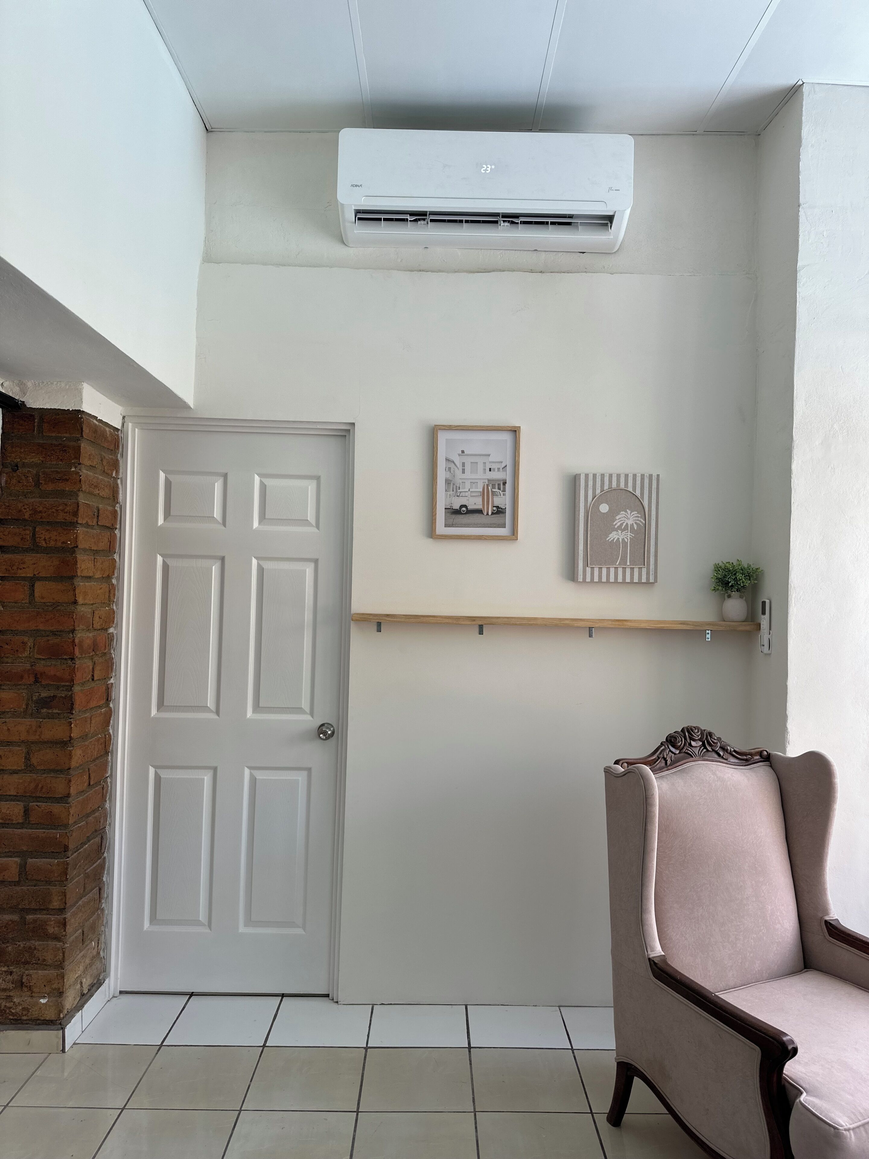 A room with a white door, an air conditioning unit, a framed picture, a shelf, and a chair.