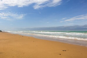 Een strand met heldere lucht, golven en iemand die wandelt.