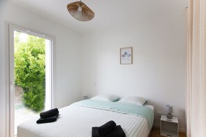 Ein Schlafzimmer mit Bett, Nachttisch, Lampe, einem gerahmten Bild und einem Fenster mit Blick auf Grünflächen.