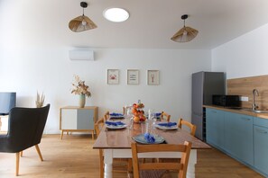 Ein Essbereich mit einem Holztisch, gedeckt für vier Personen, eine Küche mit blauen Schränken und einem schwarzen Kühlschrank.