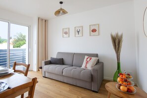 Ein Wohnzimmer mit grauem Sofa, einem Esstisch mit Stühlen und einer Vase mit Trockenpflanzen.