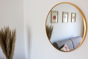 Ein runder Spiegel mit goldener Rahmung, ein graues Sofa und drei gerahmte Bilder an der Wand.
