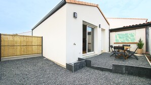Un edificio moderno con facciata bianca, una recinzione in legno, un patio in ghiaia e un tavolo con sedie.