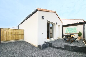Ein modernes Gebäude mit weißer Fassade, einem Holzzaun, einer gepflegten Schotterterrasse und einem Tisch mit Stühlen.