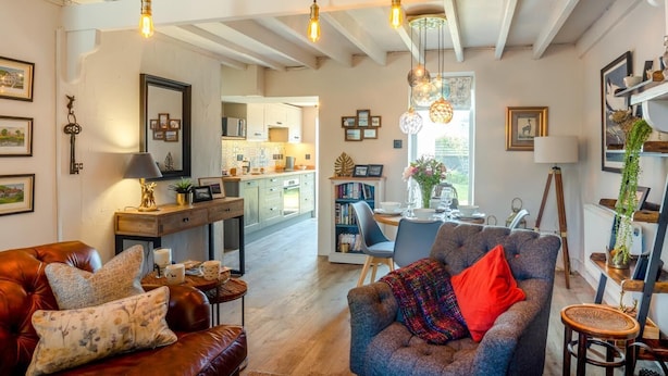 A spacious living room with a leather sofa, a blue armchair, and a dining area with a table and chairs. - 2 Bed in Rhydyclafdy (oc-b44972) (Buan)