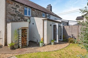 A stone house with a garden, a wooden door, and a small shed with firewood. - 2 Bed in Rhydyclafdy (oc-b44972) (Buan)