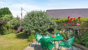 A patio with a table and chairs, surrounded by greenery and a wooden fence. - 2 Bed in Rhydyclafdy (oc-b44972) (Buan)