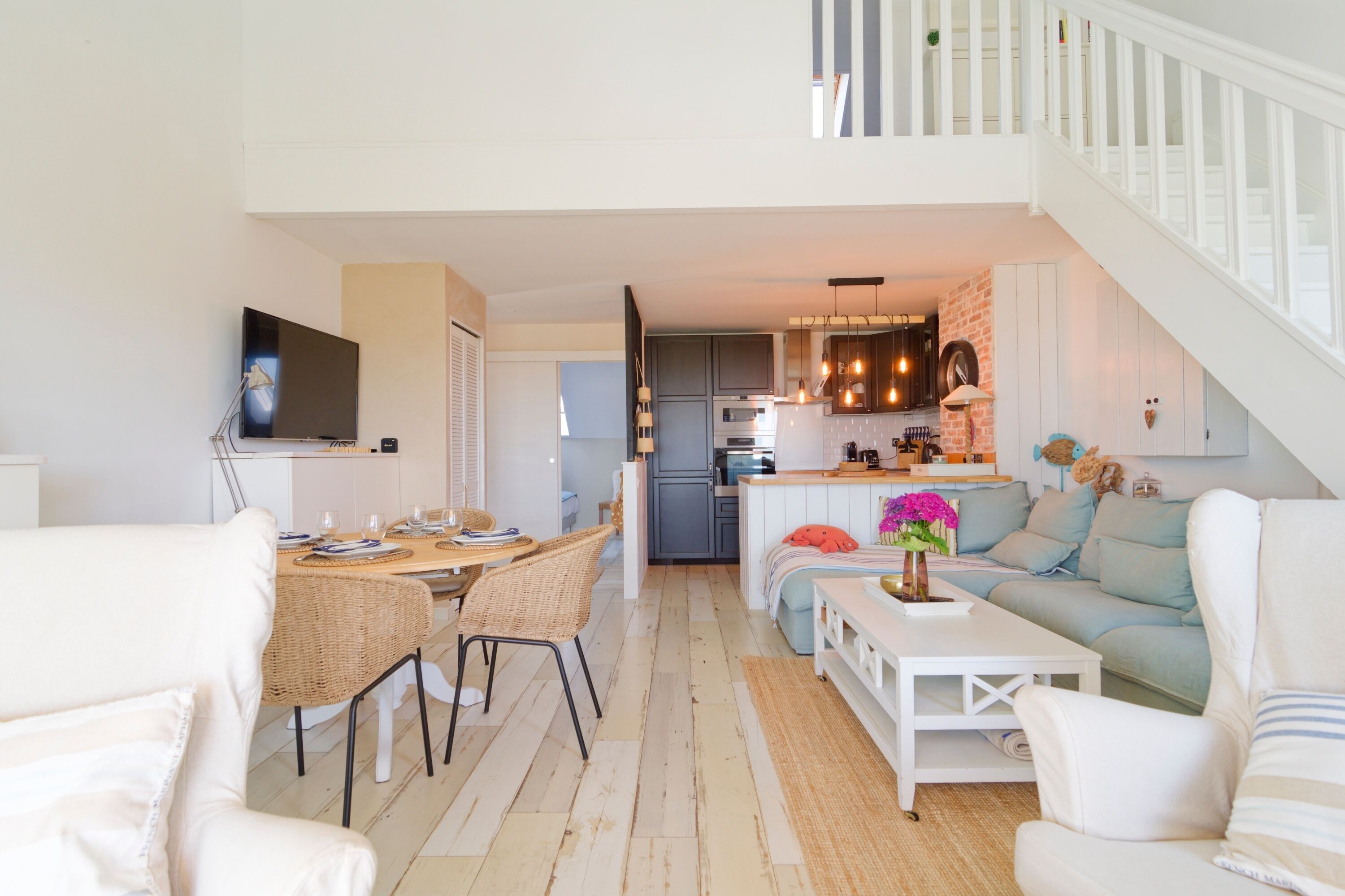 A modern living room with a dining area, kitchen, and staircase.