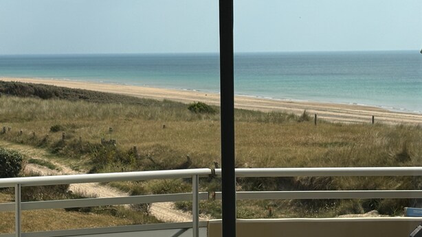Vista de uma praia a partir de uma varanda com grades, dunas gramadas e o oceano.