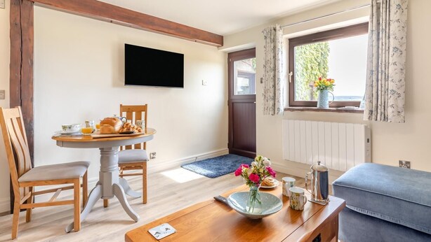 Een gezellige kamer met een houten tafel, een blauwe bank, een flatscreen televisie en een raam met gordijnen.