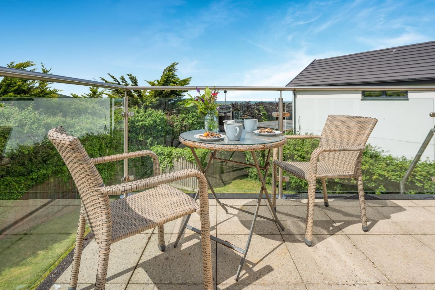 Een glazen patio met rieten stoelen en een tafel, met vrij uitzicht op het groen eromheen.
