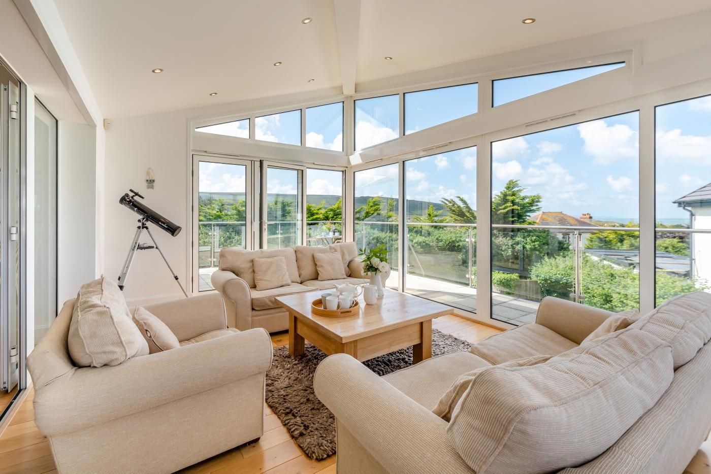 A spacious living room with large windows, a telescope, and a balcony with a view.