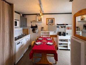 A compact kitchen with a dining table set for four, a microwave, and a stove. - Le Sommet 503 - Station de ski accessible à pied (Huez)