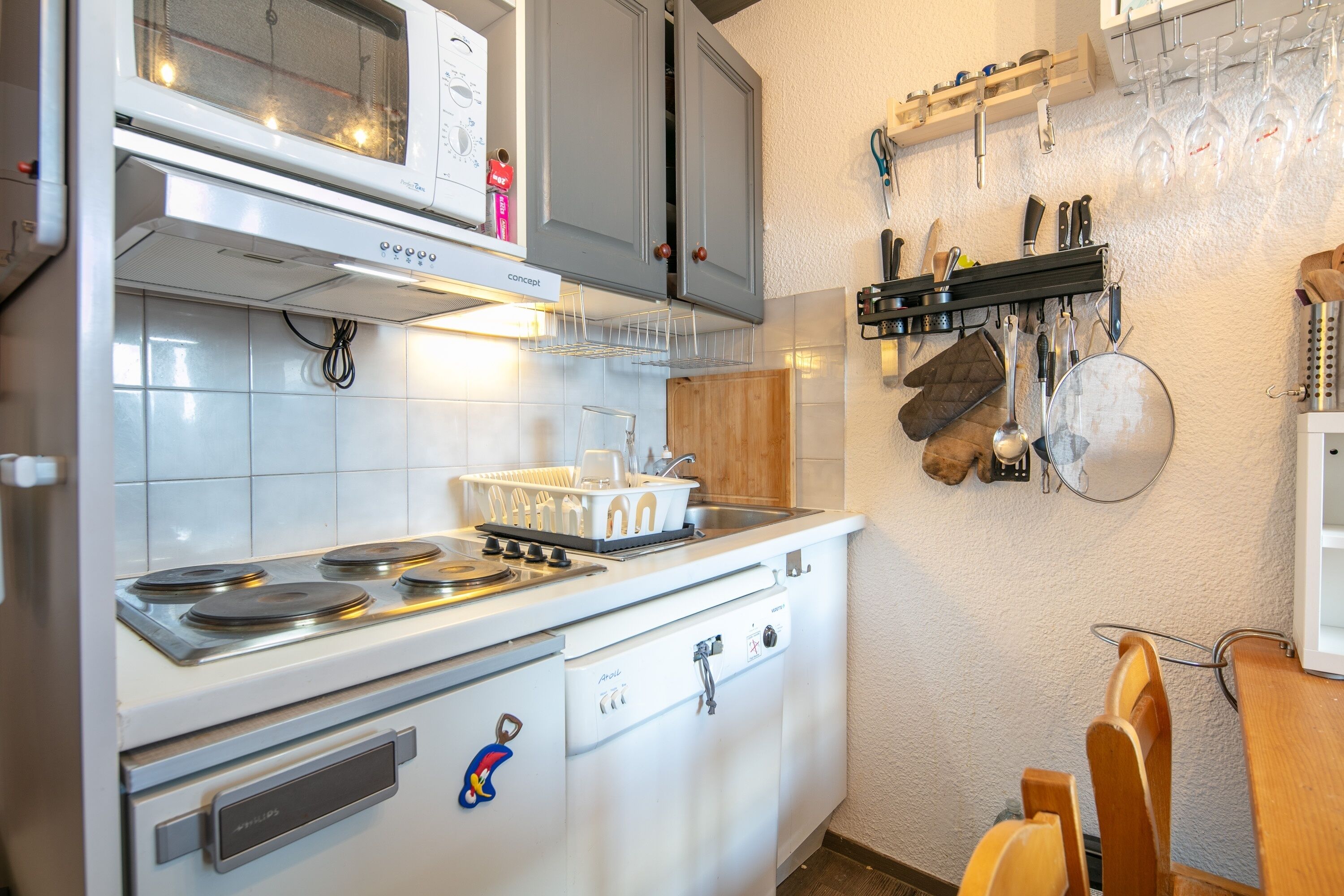 A kitchen with a stove, oven, microwave, and dishwasher. There are utensils hanging on the wall and a wooden table with chairs.