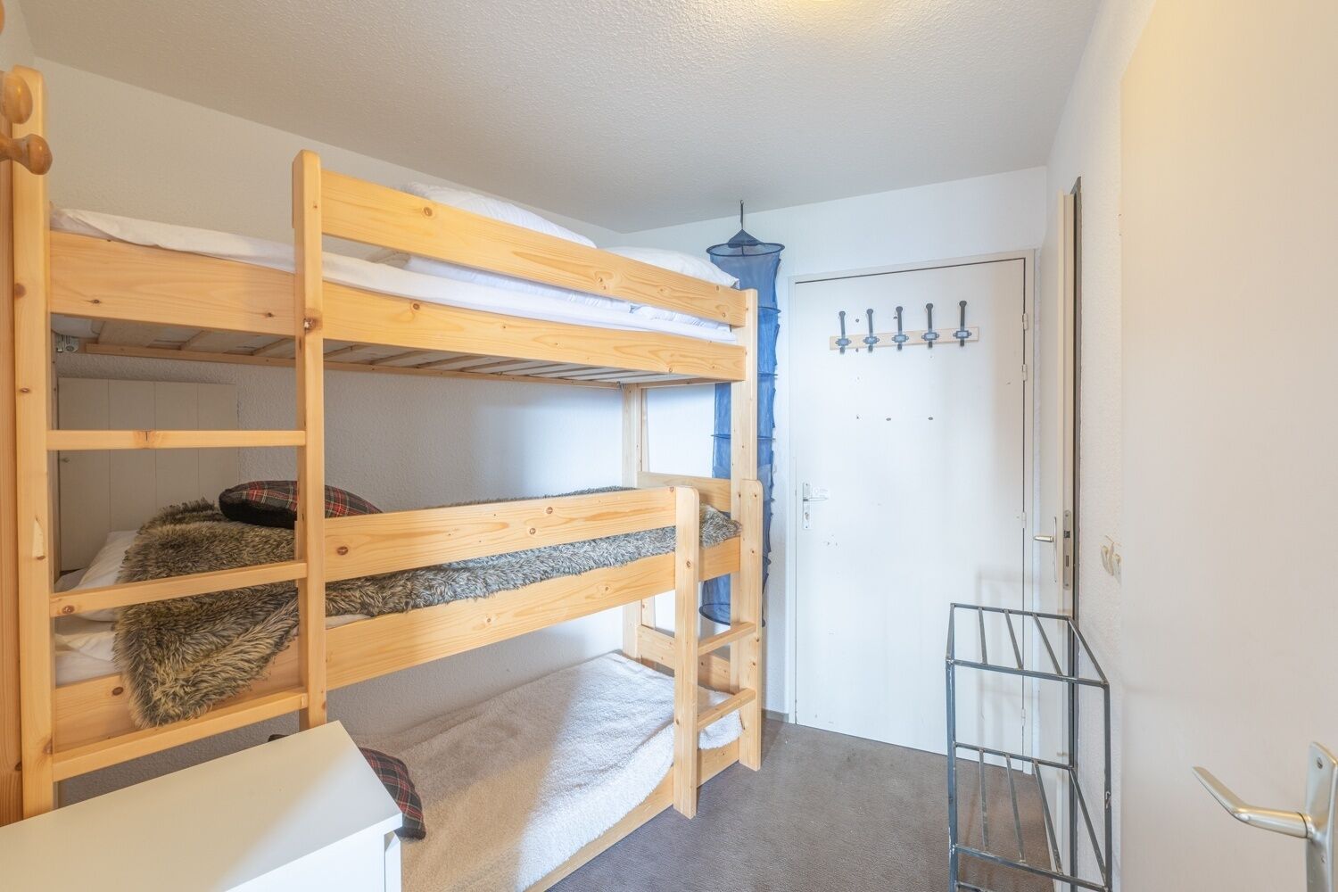 Un lit superposé avec une petite étagère et une structure métallique, une porte avec une poignée et un luminaire suspendu.