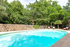 Ein Swimmingpool mit Steinmauer und üppiger Bepflanzung im Hintergrund.
