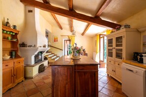 Eine Küche mit Holzbalken, Kamin, Essbereich mit Tisch und Stühlen sowie einer Treppe zu einem weiteren Raum.