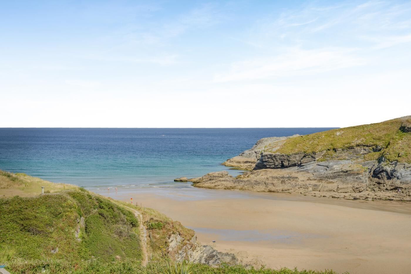 A coastal landscape with a sandy beach, rocky cliffs, and a clear sky.