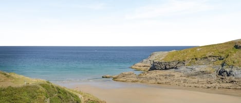 A coastal landscape with a sandy beach, rocky cliffs, and a clear sky.