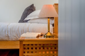 Ein ordentlich bezogenes Bett mit weißer Bettwäsche, eine Lampe auf einem hölzernen Nachttisch und ein offenes Buch auf dem Nachttisch.