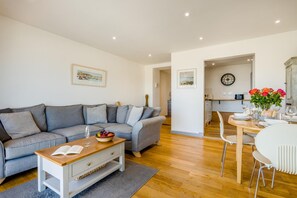 En moderne stue med en grå sofa, et træbord og et spiseområde med et hvidt bord og stole.