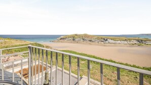 Vista costera des del balcó amb barana, una platja de sorra i roques.