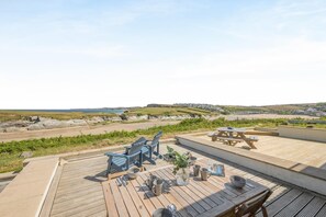 En træterrasse med siddepladser og et picnicbord med udsigt over et kystlandskab.