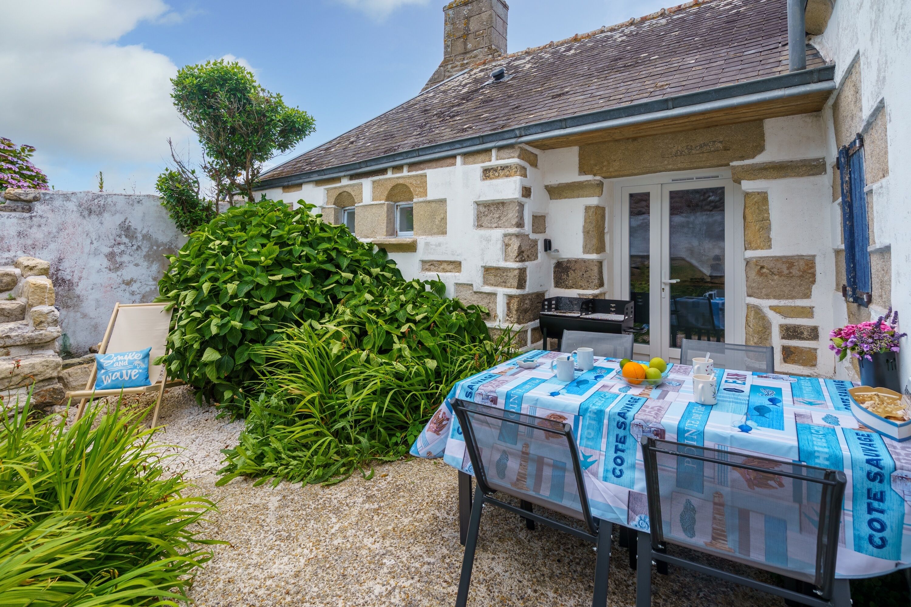 A rustic stone building with a garden area, outdoor seating, and a table with a tablecloth.
