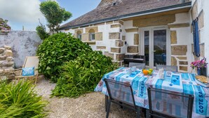 A rustic stone building with a garden area, outdoor seating, and a table with a tablecloth.