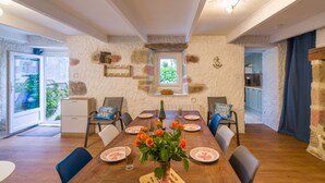 A dining area with a wooden table, chairs, a vase of flowers, and a view of the outdoors.