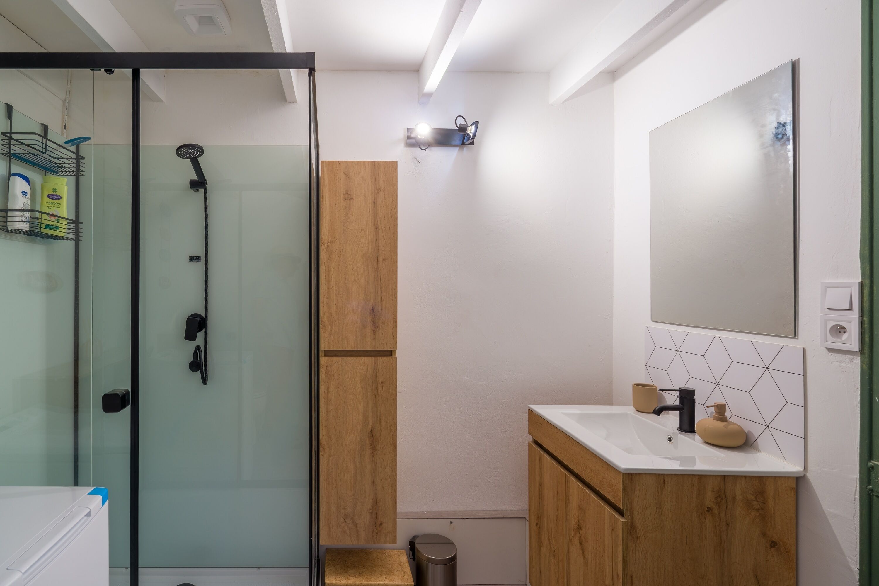 Ein Badezimmer mit Duschkabine aus Glas, einem Holzlagerfeld, einem weißen Waschbecken und einem wandmontierten Spiegel.