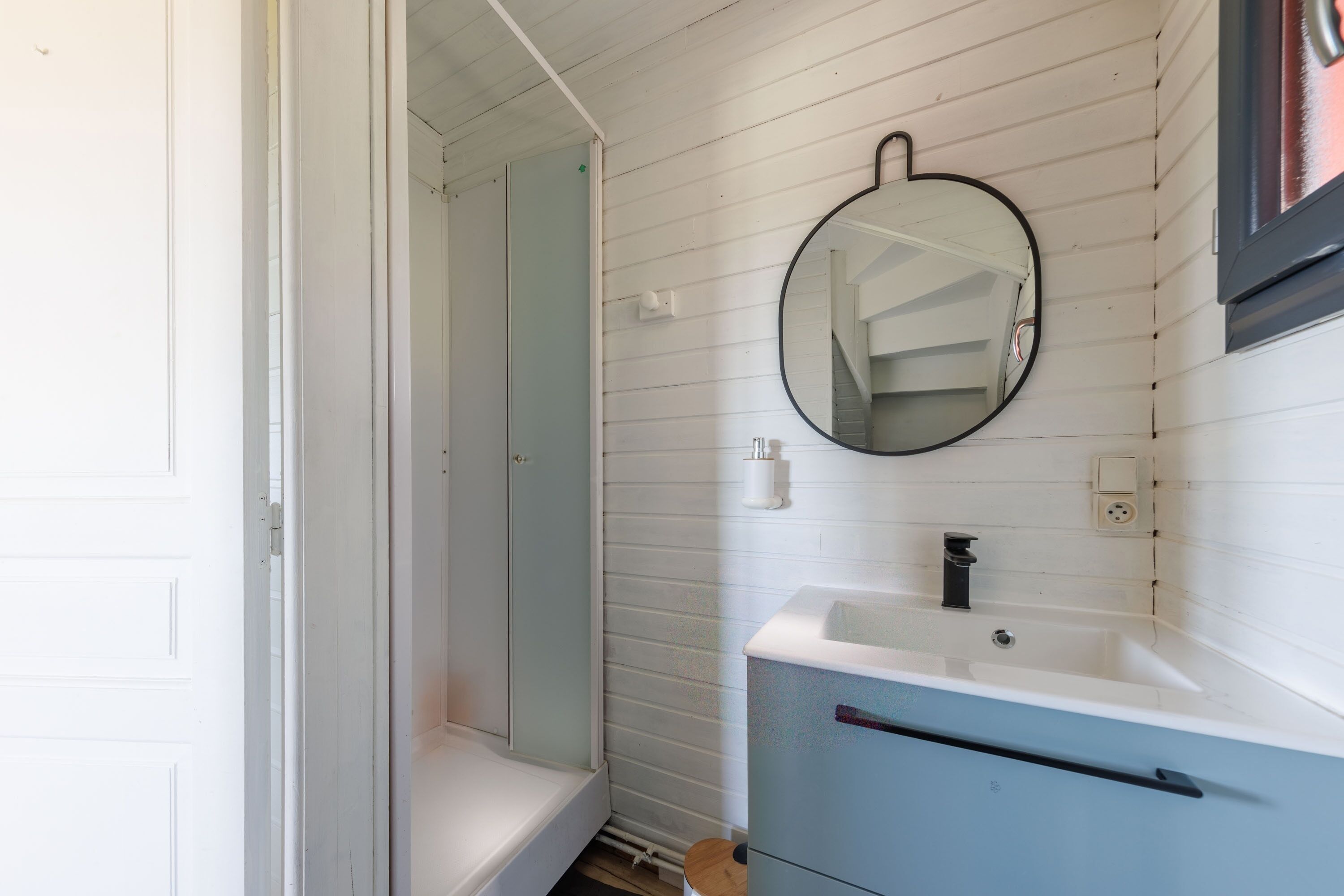A bathroom with a white vanity, a round mirror, and a shower area.