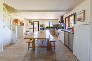 A kitchen with a wooden table, white cabinets, a washing machine, and a large window. - Les Scorios - Maison pour 10 avec beau jardin (Picherande)