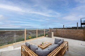 Eine Terrasse mit Meerblick, Holzmöbel und einer Backsteinmauer.