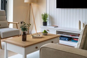 Ein modernes Wohnzimmer mit Couch, Holztisch, Stehlampe, Topfpflanze und Bücherregal mit Gesellschaftsspielen.