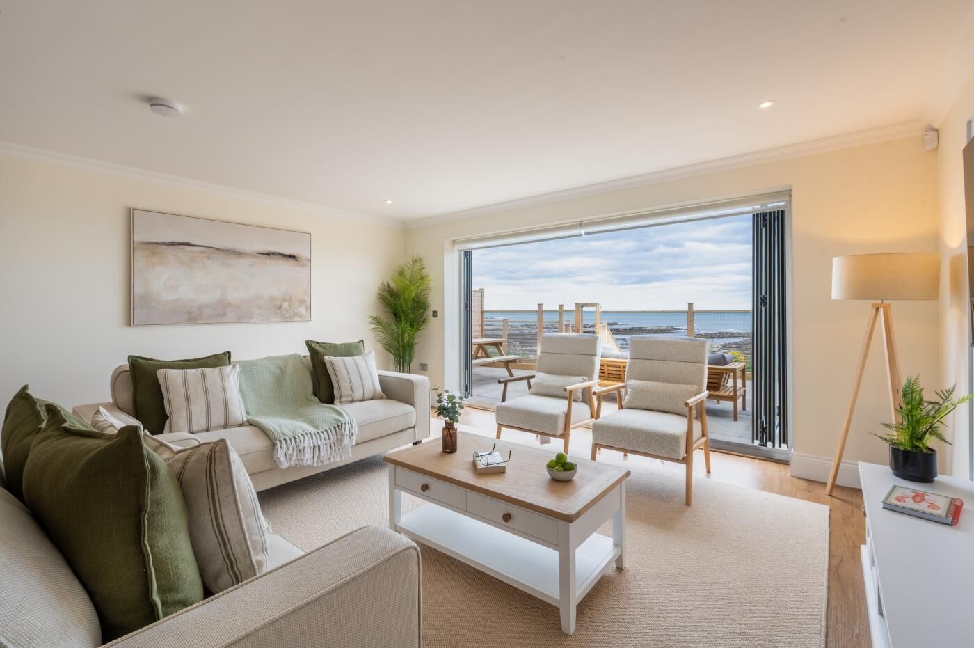 A modern living room with a sofa, armchairs, a coffee table, and a view of the sea through large windows.